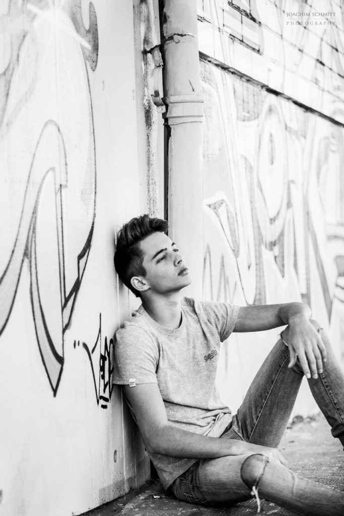 Ein junger Mann sitzt auf dem Boden vor einer Graffiti-Wand.